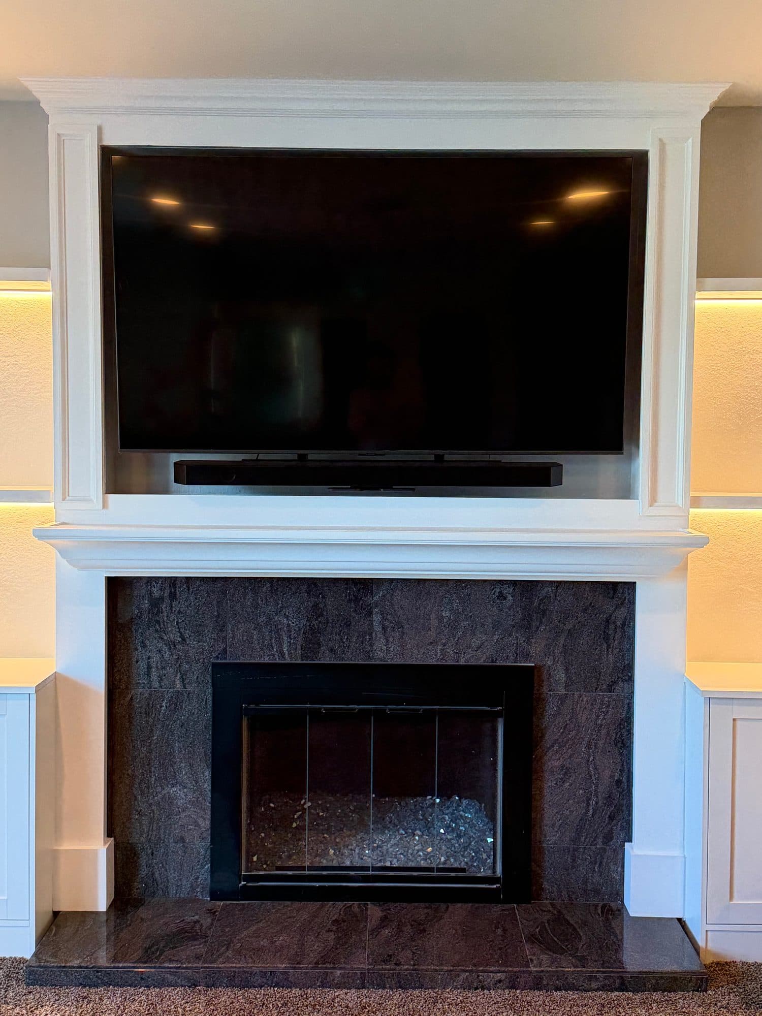 Close view of a white trimmed TV surround and mantel above a dark tile fireplace