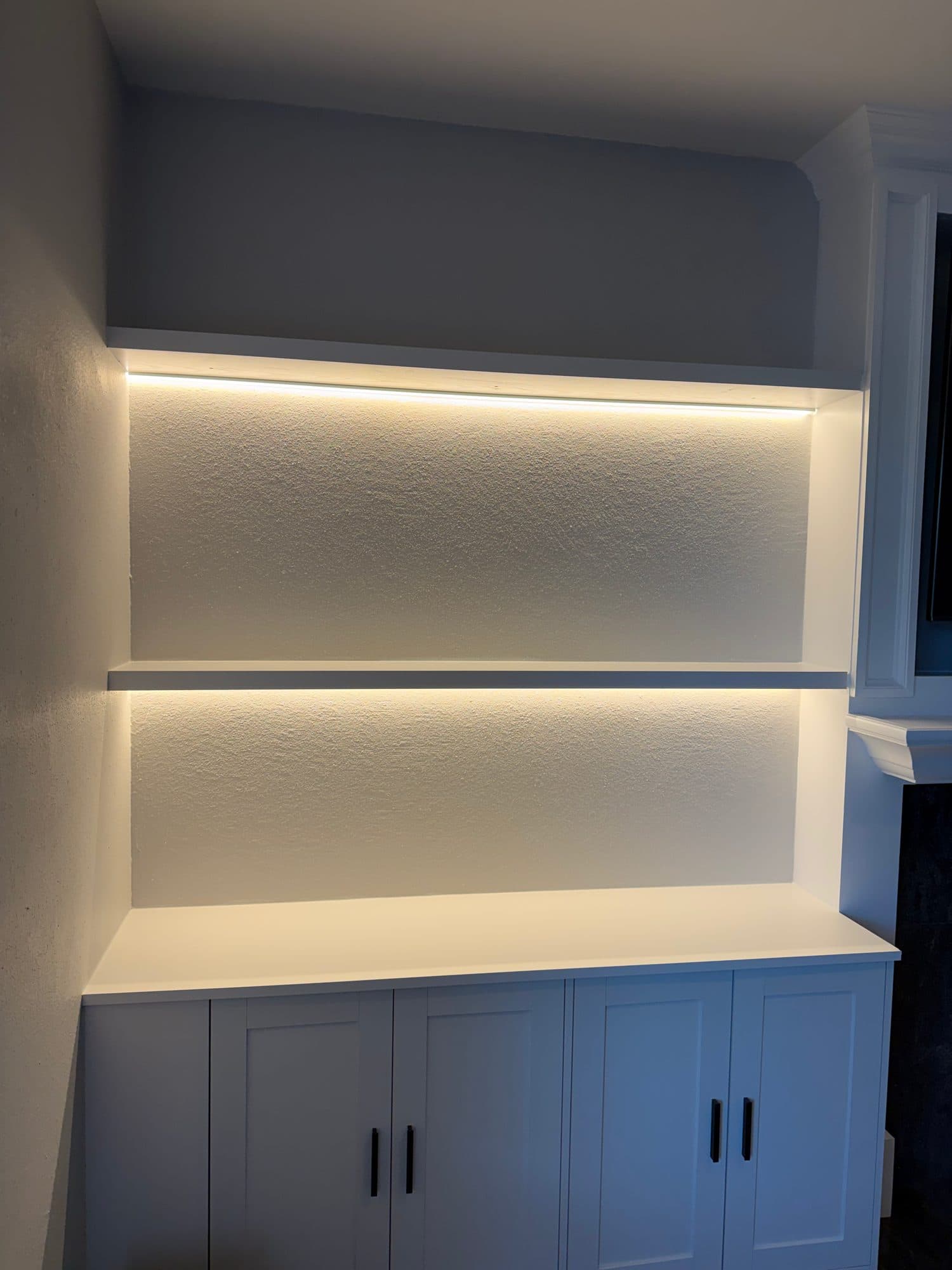 Recessed niche with two LED-lit floating shelves above white shaker base cabinets