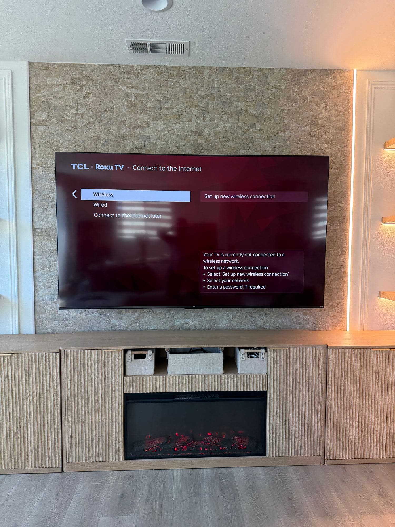 Stacked stone TV wall with vertical LED strips above a fluted wood console with built-in electric fireplace