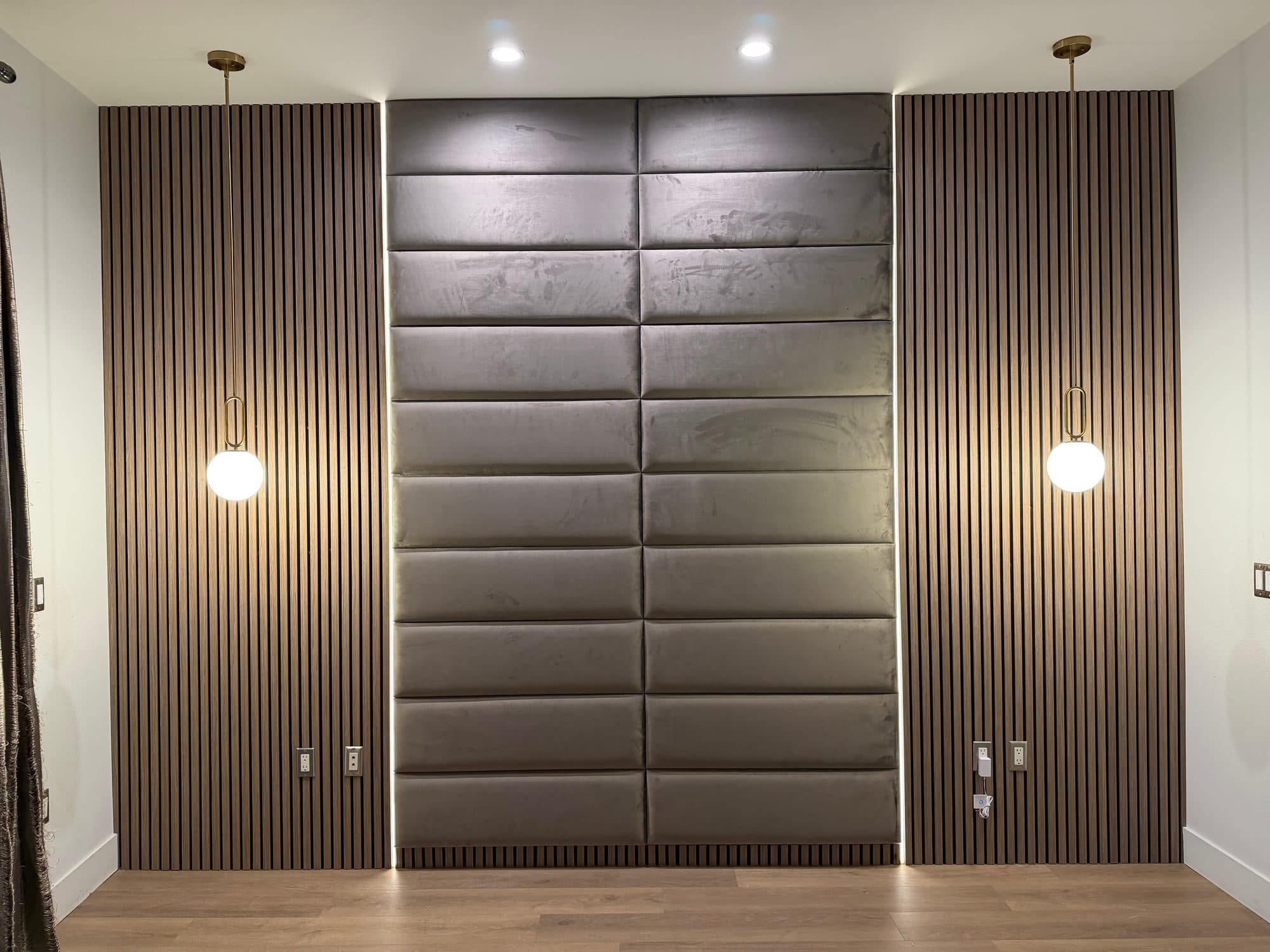 Bedroom wall with gray upholstered panels between dark wood slat sections, LED light lines and two globe pendant lights