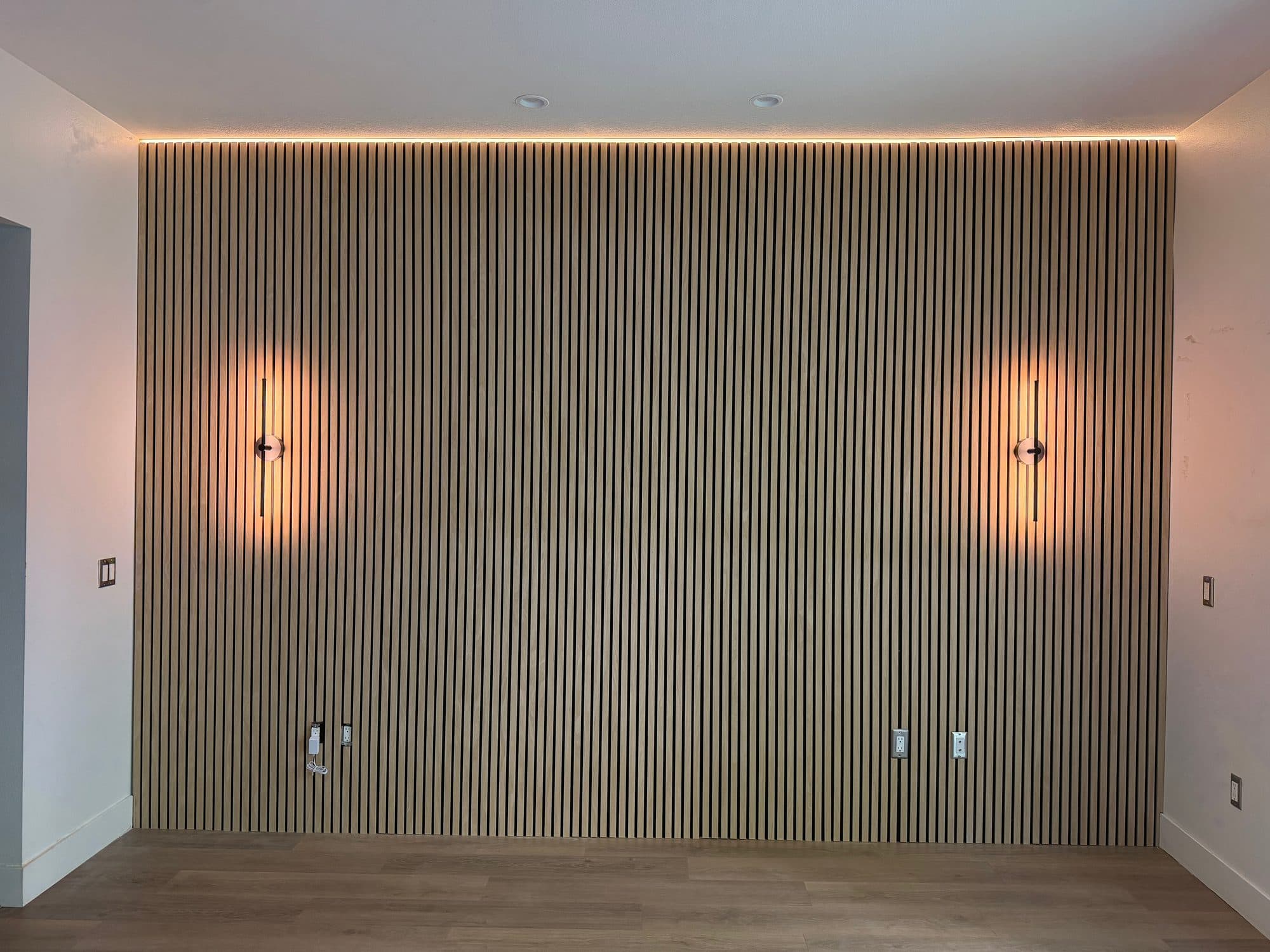Full-height wood slat accent wall with a cove LED light line along the ceiling and two vertical wall sconces