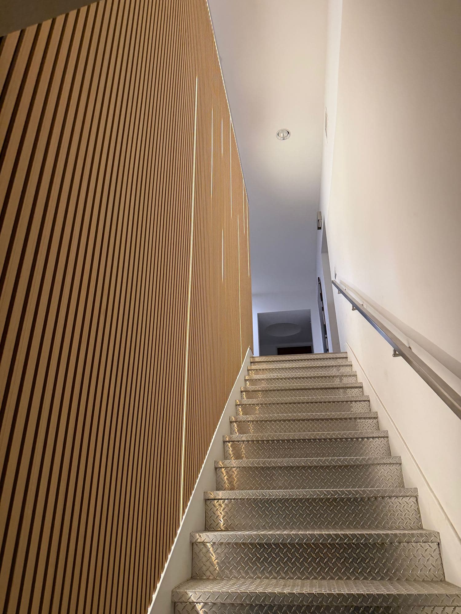 Staircase with a full-height wood slat wall and vertical LED light lines