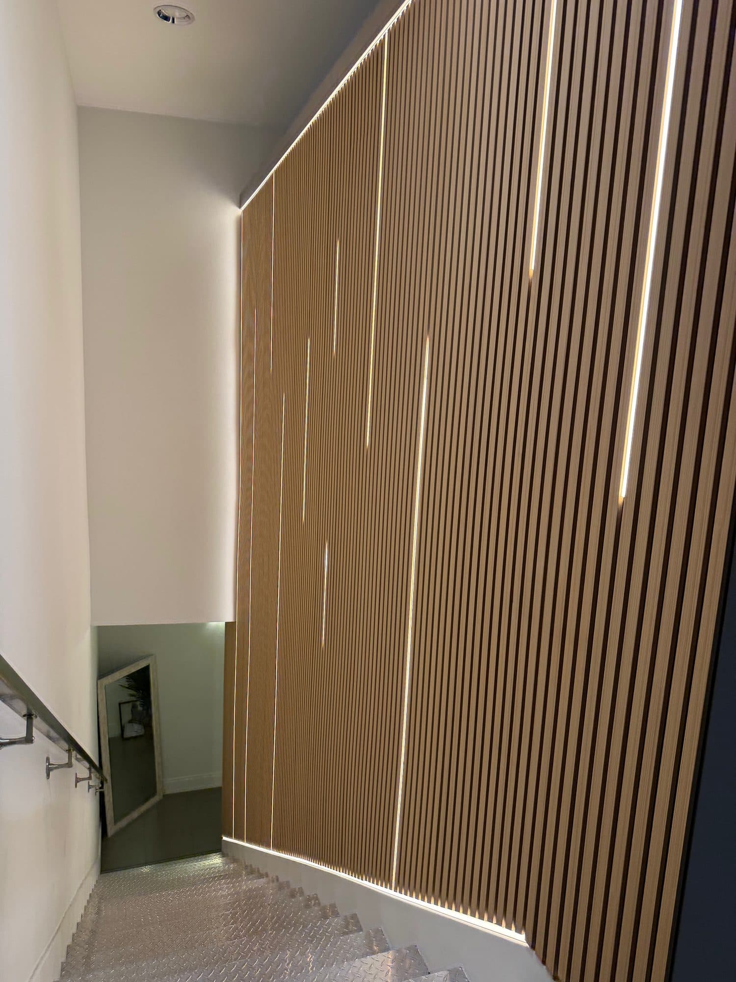 View down a staircase beside a wood slat wall with vertical and diagonal LED light lines