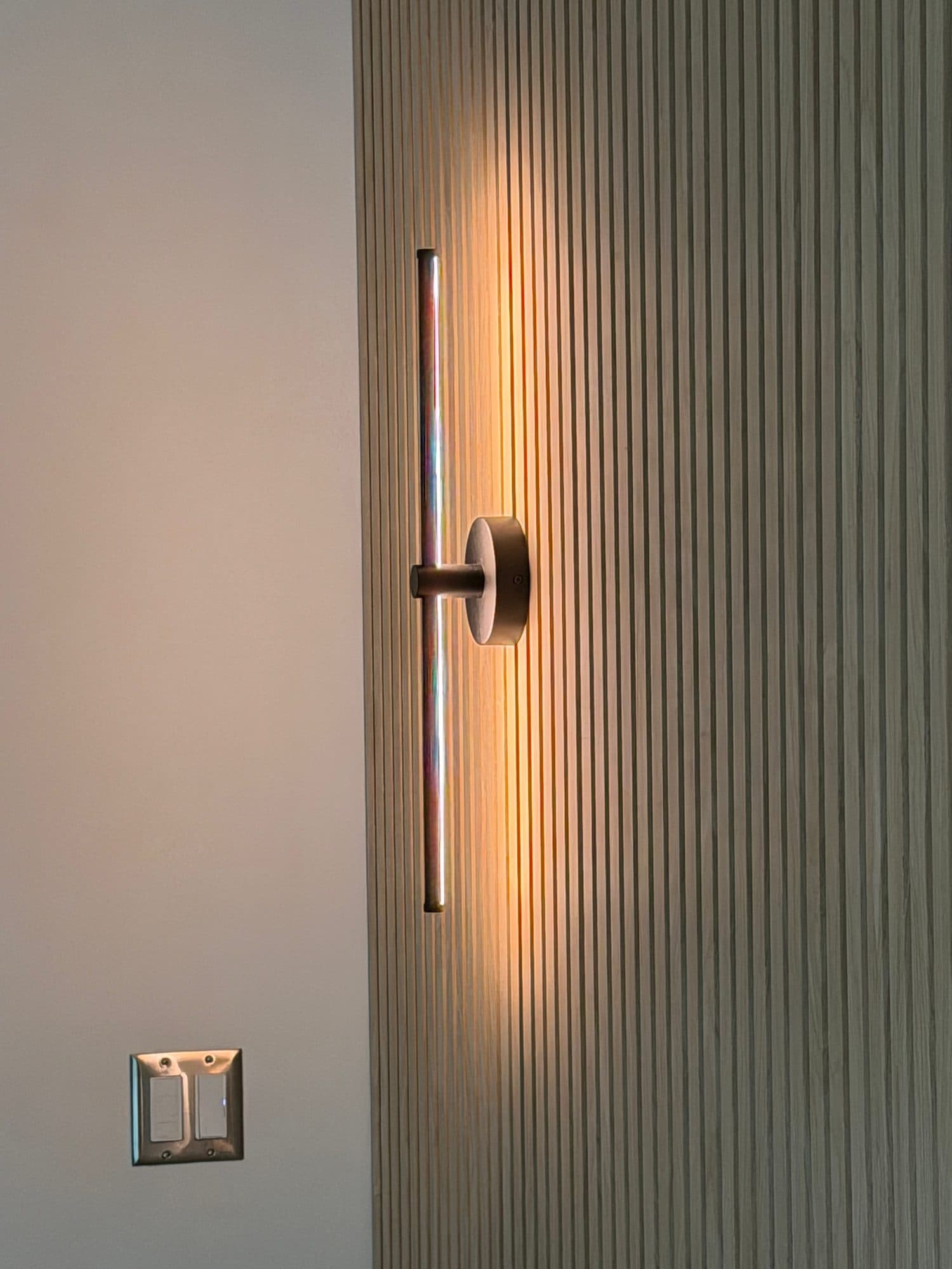 Vertical wall sconce mounted on a wood slat wall